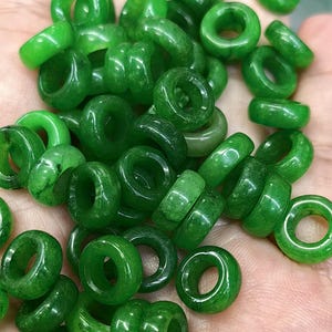 May include: A close-up of a pile of green jade donut beads. The beads are smooth and polished, with a slightly translucent appearance.