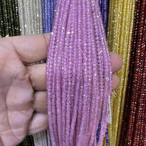Könnte beinhalten: Nahaufnahme eines Bündels rosa facettierter Edelsteinperlen. Die Perlen sind auf einem dünnen Faden aufgereiht und in einem ordentlichen, parallelen Muster angeordnet. Die Perlen sind klein und haben einen zarten, irisierenden Glanz.