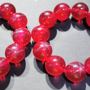 Könnte beinhalten: Zwei rote Edelstein-Armbänder mit sternförmigen Einschlüssen. Jedes Armband hat 12 runde Perlen.