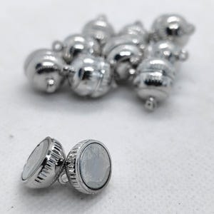 May include: A collection of shiny silver magnetic clasps, perfect for jewelry making. The clasps are round with a ridged edge and a small loop. The image shows several clasps scattered on a white surface.