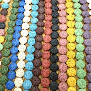 May include: A collection of round lava rock stones in a variety of colours, such as red, black, yellow, green, and blue. The stones are arranged in rows on a bamboo mat, highlighting their porous texture and natural appearance.