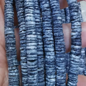 以下が含まれることがあります： 天然素材で作られたグレーとホワイトの丸いビーズのストランド。ビーズは積み重ねられており、ざらざらとした質感の表面をしています。