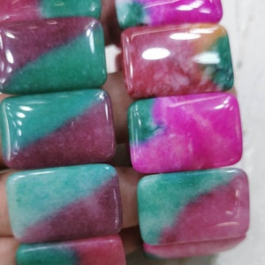 May include: A bracelet made of rectangular, multi-colored jade beads. The beads are a mix of green, pink, and white.