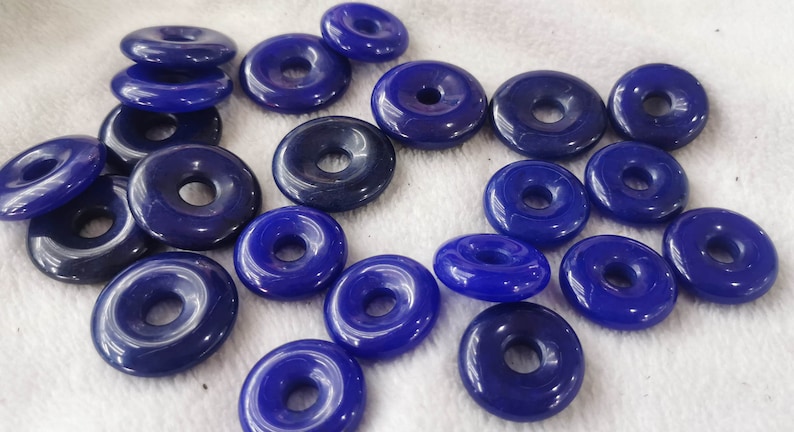 Puede incluir: Una colecci&oacute;n de 18 cuentas azules en forma de rosquilla con un agujero en el centro. Las cuentas est&aacute;n hechas de un material liso y brillante y tienen un acabado ligeramente iridiscente.