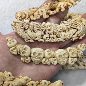 May include: Ivory-colored carved bracelets featuring various designs. One bracelet depicts skulls, another a dragon, and others show animal figures. The bracelets are intricately detailed and appear to be made of a hard material.