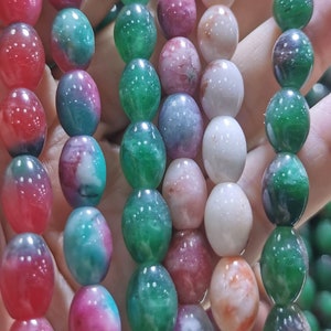 Pode incluir: Um close-up de contas ovais em tons de verde, rosa e branco. As contas são enfiadas em um cordão e estão dispostas em filas.