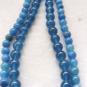 May include: Three strands of blue gemstone beads in varying shades of blue. The beads are round and appear to be polished, with a glossy finish. The beads are strung together, creating a necklace or bracelet.