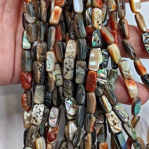 以下が含まれることがあります： 様々な茶色、灰色、オレンジの色合いの虹色のアワビ貝のビーズのストランド。ビーズは長方形で、自然で有機的な質感があります。