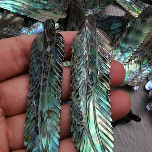 May include: Two iridescent green abalone shell feathers with a carved design. The feathers have a hole at the top for hanging.