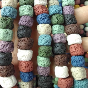 May include: A variety of lava rock beads in different colors, including white, black, brown, red, blue, green, and purple. The beads are all round and have a rough, textured surface.