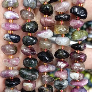May include: A strand of multi-colored gemstone beads. The beads are a mix of pink, green, black, and white. The beads are tumbled and have a smooth, polished finish.