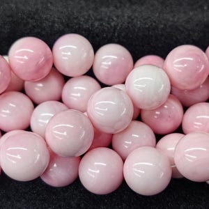 May include: A close-up of a strand of pink and white beads. The beads are round and polished, with a glossy finish. They are strung together, creating a tactile surface. These beads are suitable for jewellery making and have a soft, feminine appearance.