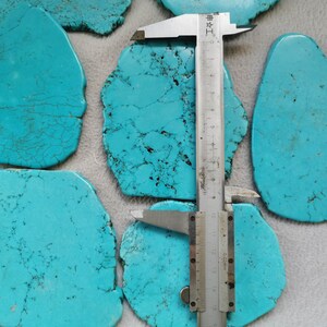 May include: A close-up of turquoise cabochons, some with a rough texture, measured with a ruler. The ruler is marked in centimeters.