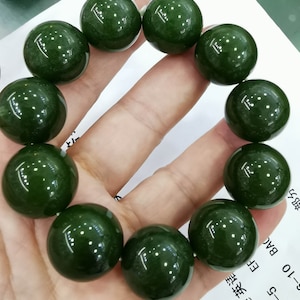 May include: A green jade bracelet with ten round beads. The bracelet is on a person's hand.