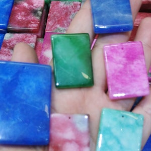 May include: Six rectangular shaped polished stones in various colors, including blue, green, pink, and red. The stones have a marbled appearance and are arranged on a hand.