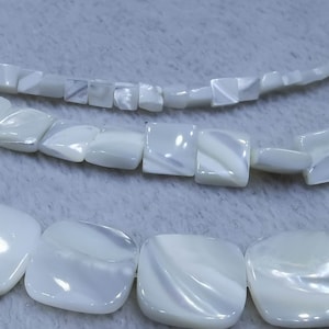 May include: Three strands of white shell beads, with the bottom strand featuring larger, square-shaped beads.