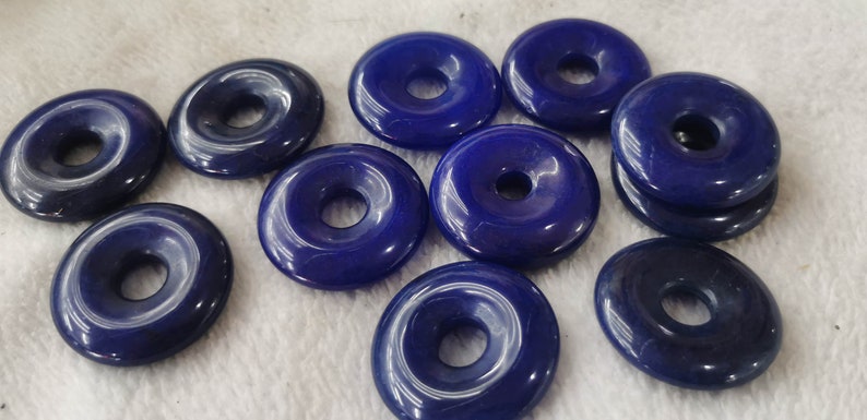 Puede incluir: Diez cuentas de piedra preciosa de color azul oscuro en forma de rosquilla con un agujero en el centro. Las cuentas son lisas y pulidas.
