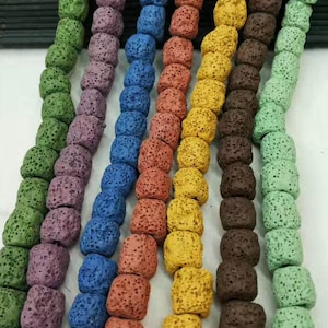 Puede incluir: Una variedad de cuentas de roca volcánica en diferentes colores, incluyendo verde, morado, azul, marrón y amarillo. Las cuentas son todas redondas y tienen una superficie rugosa y texturizada.