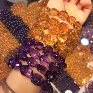 Op de afbeelding: Twee armbanden gemaakt van gefacetteerde edelsteen kralen. De ene armband is gemaakt van paarse amethist kralen en de andere van oranje citrien kralen.