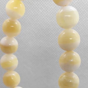 May include: A string of spherical, cream-coloured beads with a marbled, yellow-white pattern. The beads are strung on a thin, silver-coloured wire, forming a bracelet or necklace.