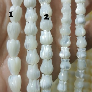 Puede incluir: Cuatro hebras de cuentas de concha blanca con un diseño en forma de flor. Las cuentas están enhebradas en un hilo transparente. Las cuentas tienen aproximadamente 1 cm de diámetro.