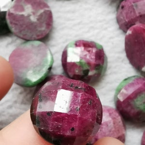 May include: A close-up of a faceted, pink and green gemstone. The gemstone is round and has a polished finish. It is being held by a finger.