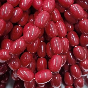 May include: A large collection of glossy, oval-shaped beads in a deep, vibrant red color. Each bead features a smooth, reflective surface and is strung together on a thin white cord, creating a dense, textured cluster of uniform red components.