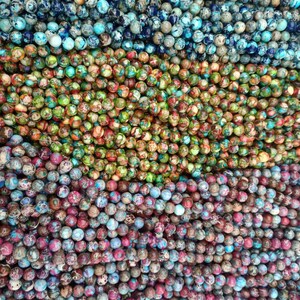 May include: A close-up of a variety of colorful round beads. The beads are made of a mottled stone with shades of blue, green, brown, and red. The beads are arranged in rows, creating a visually appealing pattern.
