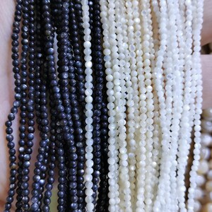 May include: A close-up of two strands of beads. One strand is made of black beads and the other is made of white beads. Both strands are made of small, round beads.