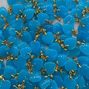 May include: A collection of light blue heart-shaped pendants with gold-colored accents. The pendants are scattered across the surface, showcasing their glossy finish and delicate design. The gold accents add a touch of elegance to the overall aesthetic.