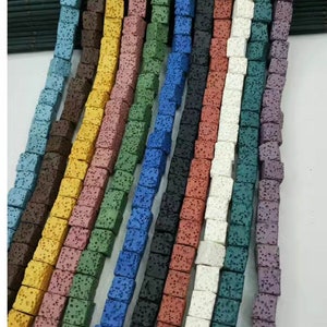 May include: Assortment of lava rock beads in various colours, including blue, green, yellow, brown, and white. The beads are square shaped and have a rough, textured surface.