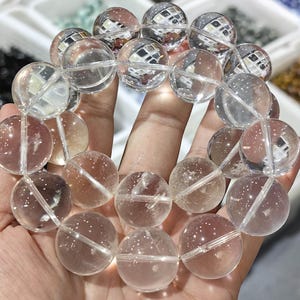 Puede incluir: Un brazalete de cuentas de cristal de cuarzo transparente con cuentas grandes y redondas. Las cuentas son lisas y pulidas, y tienen un ligero brillo.