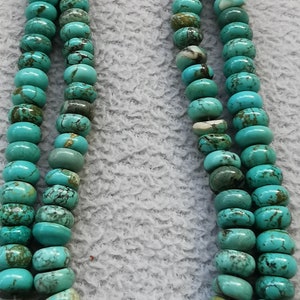 May include: A strand of turquoise beads, featuring a mix of light and dark blue tones, with brown and black marbling. The beads are round and have a smooth, polished finish.
