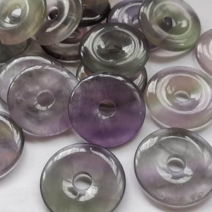 May include: A collection of purple, green, and clear donut-shaped gemstone beads with a hole in the center.