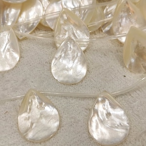 May include: A strand of white mother of pearl teardrop beads. The beads are strung on a clear elastic cord.