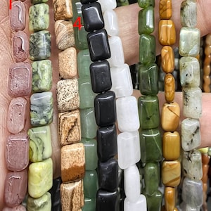 May include: Nine strands of square-shaped gemstone beads in various colors, including green, brown, black, white, and pink. The beads are arranged in a vertical line, with the top of each strand aligned.