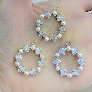 May include: Three gold and silver pendant charms with a circle design. Each charm is adorned with a row of white pearls and clear square-shaped rhinestones.