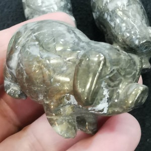 Puede incluir: Una pequeña figurita de cerdo dorada hecha de pirita. La figurita tiene una superficie detallada y texturizada y es una opción popular para la decoración del hogar o como regalo.