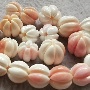 May include: A strand of white and pink shell beads with a flower-like design. The beads are strung together and are ready to be used for jewellery making.