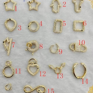 May include: Assortment of 15 gold-tone charm pendants with clear crystal embellishments. The charms include a star, a hand, a cross, a circle, a rectangle, a lightning bolt, a heart, an infinity symbol, and more.