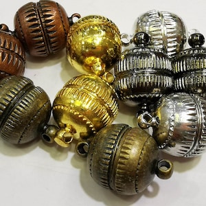 May include: A group of eight round metal beads with decorative patterns. The beads are in various shades of gold, silver, and copper. Each bead has a small loop on the top for attaching to a string or chain.