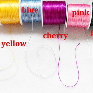 May include: Spools of elastic cord in various colours, including black, white, yellow, blue, cherry, pink, green, and dark green. The cords are arranged in a row, with the colours labelled below each spool.
