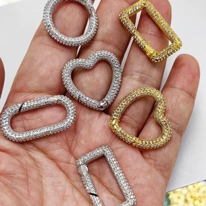 May include: Six different styles of silver and gold-toned jewelry clasps, each encrusted with clear rhinestones. The clasps are in the shapes of a circle, rectangle, heart, and oval.