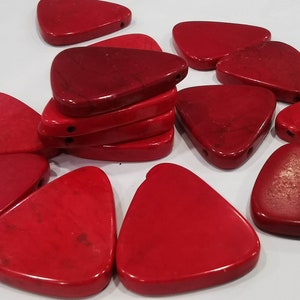 Puede incluir: Un grupo de colgantes de piedra de forma triangular roja con un agujero perforado en la parte superior. Los colgantes están hechos de una piedra lisa y pulida con un patrón de mármol.