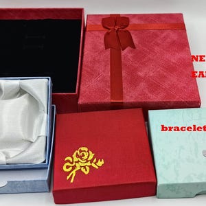 Puede incluir: Cuatro cajas de regalo para joyas. Las cajas son rojas, azules y verdes. Las cajas tienen un diseño de rosa y las palabras "NECKLACE EARRINGS" y "bracelet/bangle" impresas en ellas.