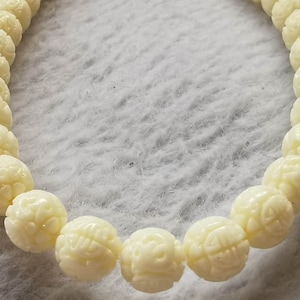 Peut inclure: Un bracelet blanc en perles avec des sculptures complexes sur chaque perle.