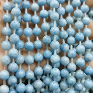 May include: A strand of light blue aquamarine beads. The beads are round and smooth, and they are strung on a clear elastic cord.