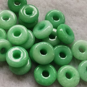 May include: A pile of green jade donut beads with a hole in the center. The beads are smooth and polished.