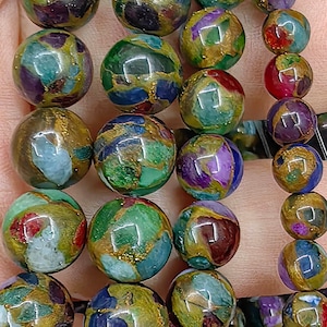 May include: A strand of colourful round beads with gold flecks. The beads are made from a variety of materials, including glass, stone, and metal. The beads are strung on a clear elastic cord.