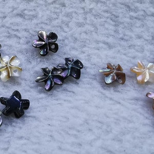 May include: Assortment of shell flower-shaped buttons in various shades of black, brown, and white.